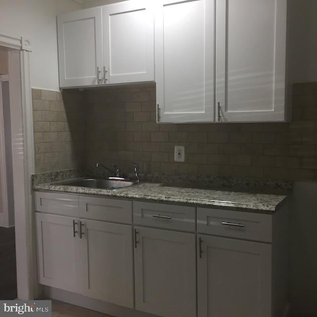 kitchen featuring sink, backsplash, white cabinets, and light stone counters