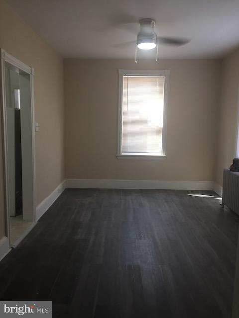 empty room with dark hardwood / wood-style floors, radiator heating unit, and ceiling fan