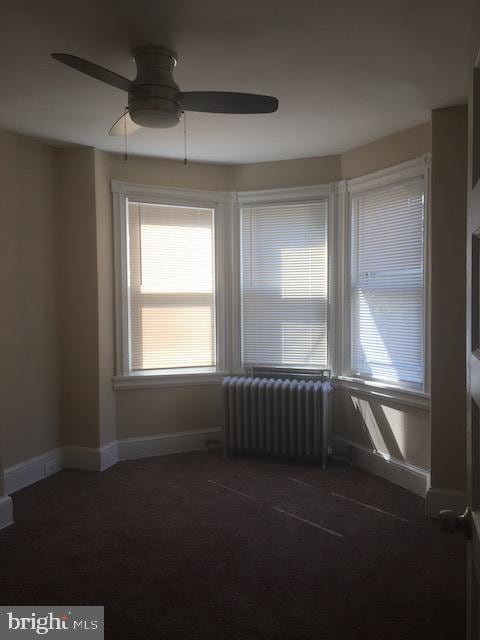 spare room with dark carpet, radiator heating unit, and ceiling fan