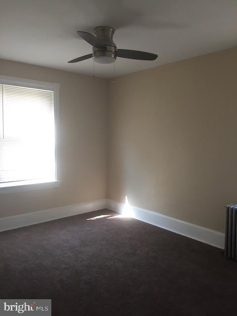 carpeted empty room featuring ceiling fan and radiator