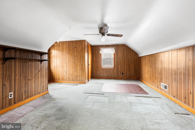 additional living space featuring vaulted ceiling, light colored carpet, wooden walls, and ceiling fan