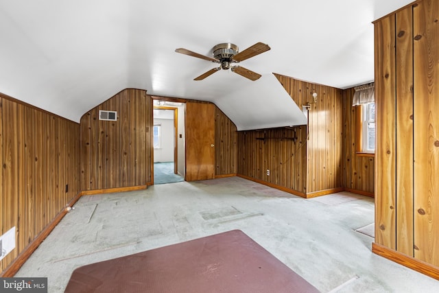 additional living space featuring light carpet, vaulted ceiling, ceiling fan, and wood walls