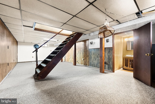 basement with carpet, a drop ceiling, and wooden walls