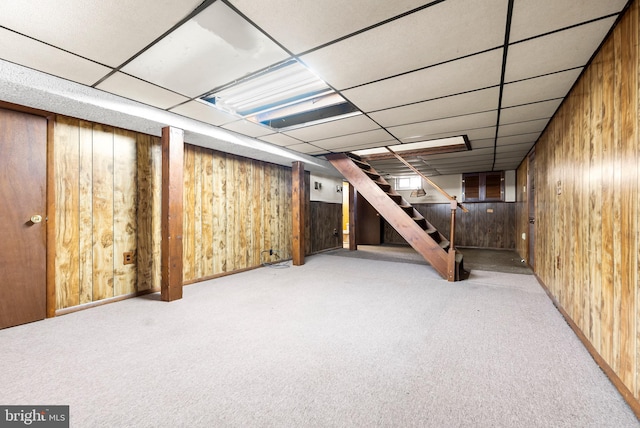 basement with carpet, a paneled ceiling, and wooden walls