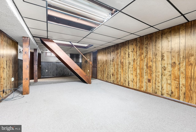 basement with carpet flooring, a paneled ceiling, and wood walls