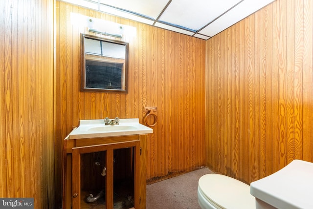 bathroom featuring vanity, wooden walls, and toilet