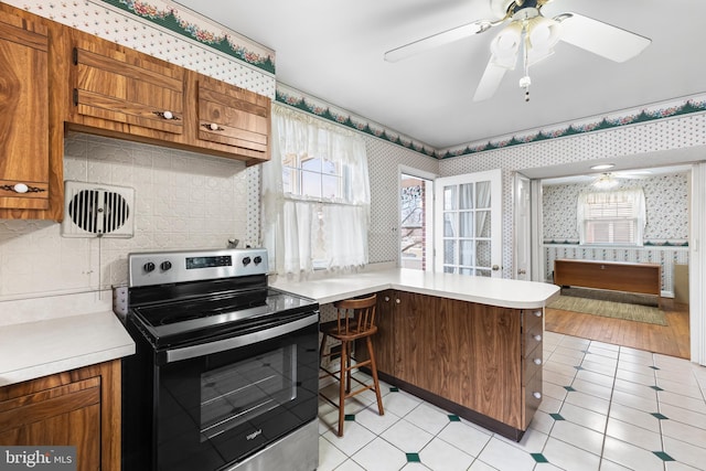 kitchen featuring backsplash, stainless steel range with electric cooktop, kitchen peninsula, and ceiling fan