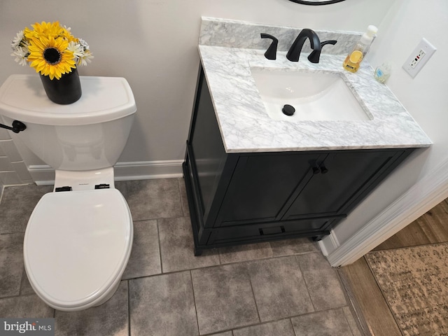 half bathroom featuring vanity, toilet, and baseboards