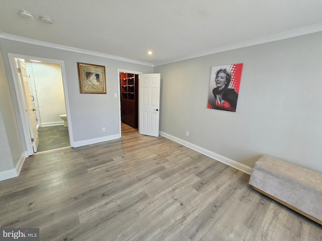 unfurnished bedroom featuring a spacious closet, wood finished floors, baseboards, and ornamental molding