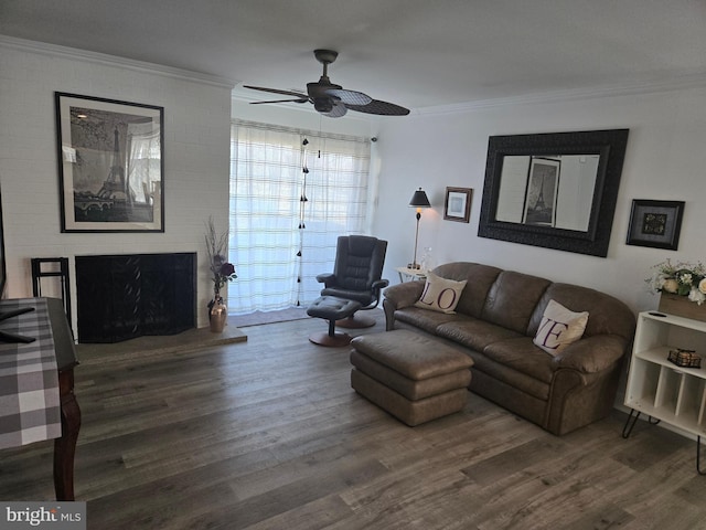 living room featuring a brick fireplace, crown molding, a ceiling fan, and wood finished floors