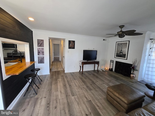 living room with ceiling fan, a fireplace with raised hearth, wood finished floors, and crown molding