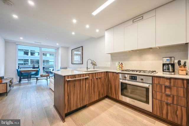 kitchen featuring sink, white cabinetry, light wood-type flooring, kitchen peninsula, and stainless steel appliances