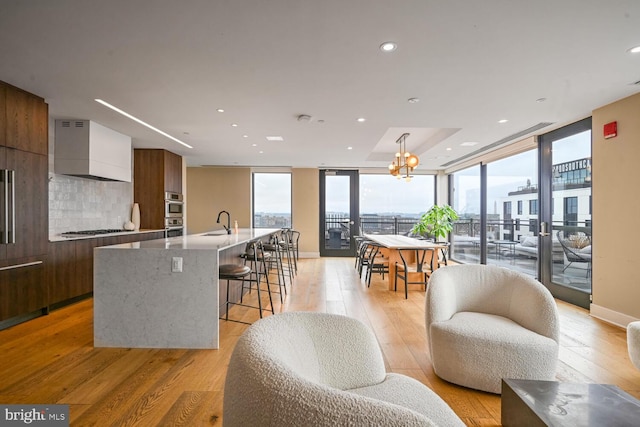 kitchen with light wood-type flooring, appliances with stainless steel finishes, an island with sink, and wall chimney range hood