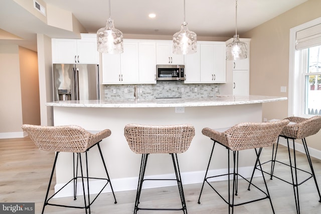 kitchen with a breakfast bar, appliances with stainless steel finishes, white cabinetry, light stone countertops, and an island with sink