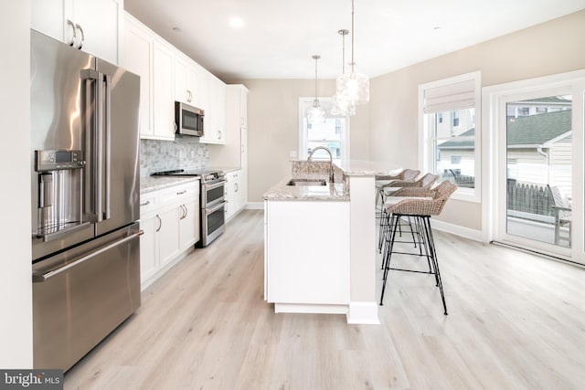 kitchen featuring sink, hanging light fixtures, a center island with sink, stainless steel appliances, and white cabinets