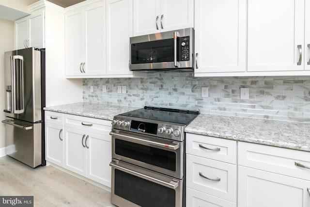 kitchen with stainless steel appliances, tasteful backsplash, white cabinets, and light stone counters