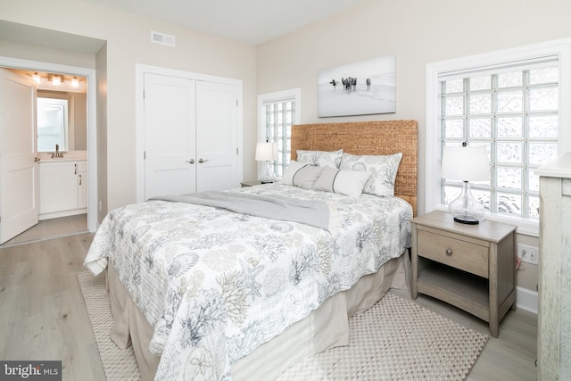 bedroom with light hardwood / wood-style flooring, ensuite bath, and a closet