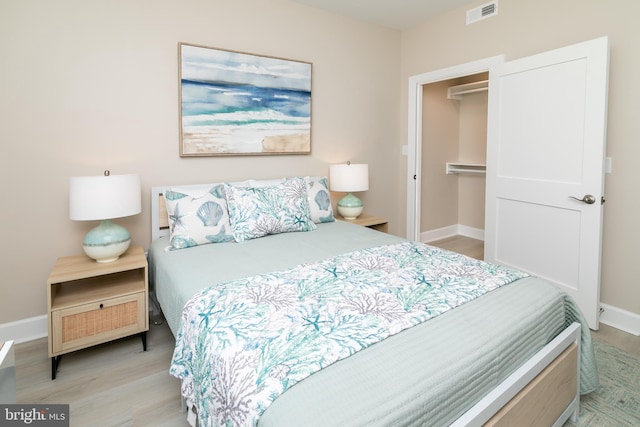 bedroom featuring a walk in closet, light hardwood / wood-style floors, and a closet