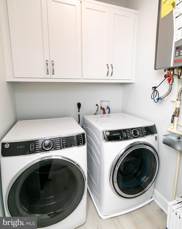 clothes washing area with light hardwood / wood-style floors, washing machine and dryer, cabinets, and tankless water heater