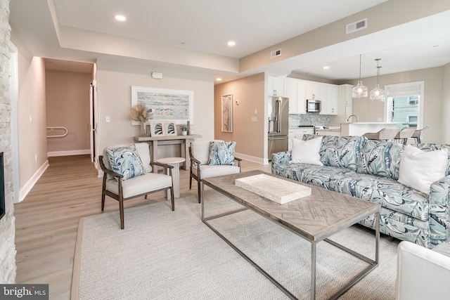 living room with sink, a raised ceiling, and light wood-type flooring