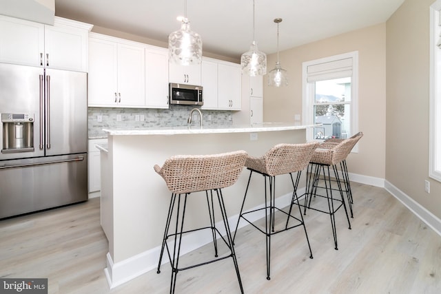 kitchen with pendant lighting, appliances with stainless steel finishes, white cabinetry, backsplash, and an island with sink