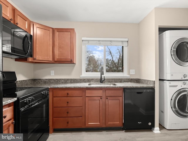 kitchen featuring sink, light hardwood / wood-style flooring, dark stone countertops, stacked washer / dryer, and black appliances