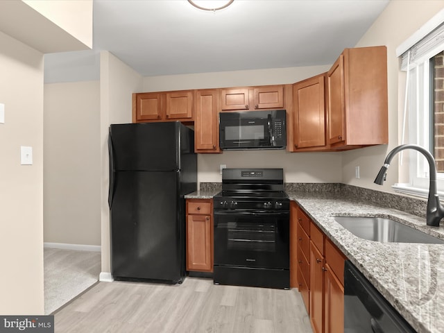 kitchen with light stone countertops, sink, light hardwood / wood-style floors, and black appliances