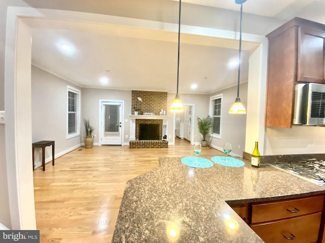 kitchen with light hardwood / wood-style flooring, dark stone countertops, hanging light fixtures, a fireplace, and stainless steel gas stovetop