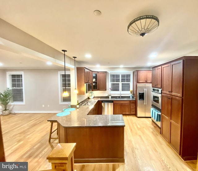 kitchen featuring appliances with stainless steel finishes, stone countertops, decorative light fixtures, light hardwood / wood-style floors, and kitchen peninsula