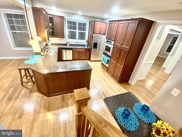 kitchen featuring appliances with stainless steel finishes, a kitchen bar, light wood-type flooring, and dark stone countertops