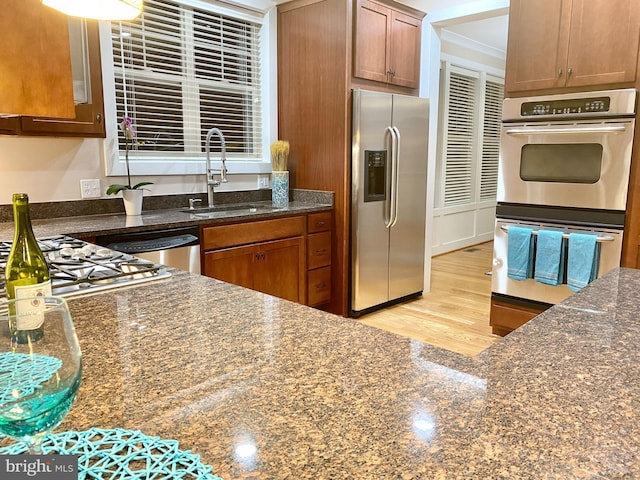 kitchen featuring stainless steel appliances, light hardwood / wood-style floors, sink, and dark stone counters