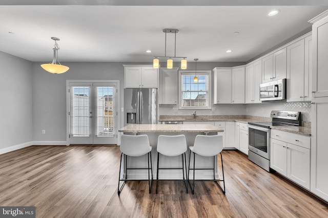 kitchen with white cabinetry, a center island, a kitchen breakfast bar, pendant lighting, and stainless steel appliances