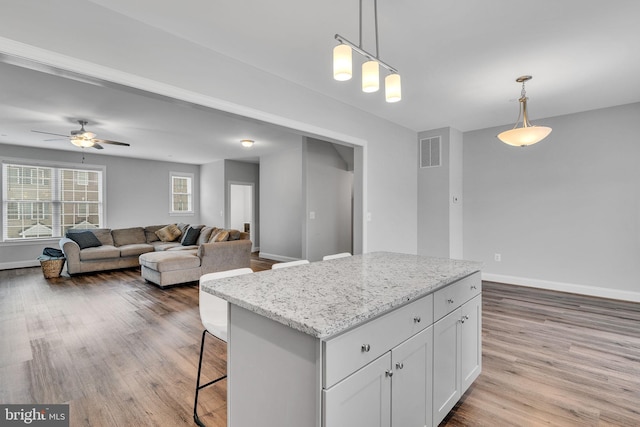 kitchen with pendant lighting, light stone countertops, a center island, and white cabinets