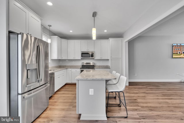 kitchen with white cabinetry, stainless steel appliances, decorative light fixtures, and a center island