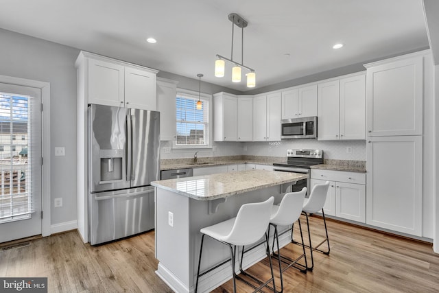 kitchen with pendant lighting, sink, white cabinetry, stainless steel appliances, and a center island