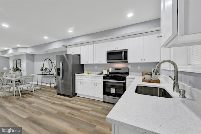 kitchen featuring sink, light hardwood / wood-style flooring, appliances with stainless steel finishes, light stone counters, and white cabinets