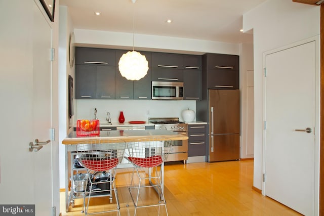 kitchen with light wood finished floors, stainless steel appliances, modern cabinets, decorative light fixtures, and light countertops