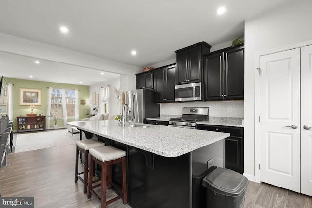 kitchen featuring a breakfast bar, a center island with sink, stainless steel appliances, open floor plan, and dark cabinets