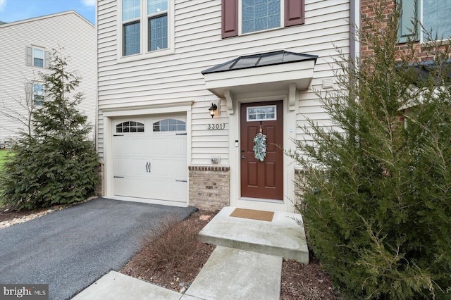 entrance to property featuring aphalt driveway, brick siding, an attached garage, a standing seam roof, and metal roof