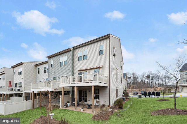 rear view of property featuring a lawn, fence, a wooden deck, and a patio