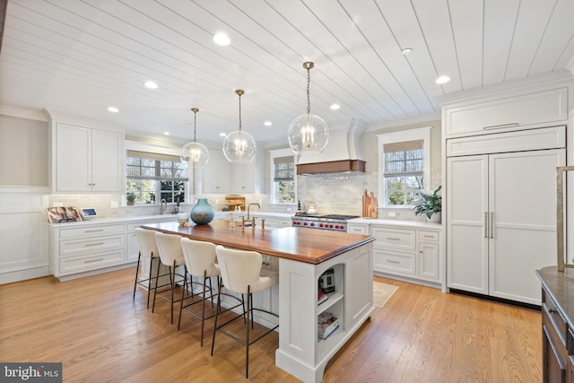 kitchen featuring hanging light fixtures, wooden counters, an island with sink, and white cabinets