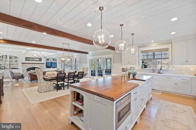 kitchen with white cabinetry, hanging light fixtures, stainless steel microwave, a healthy amount of sunlight, and a kitchen island with sink