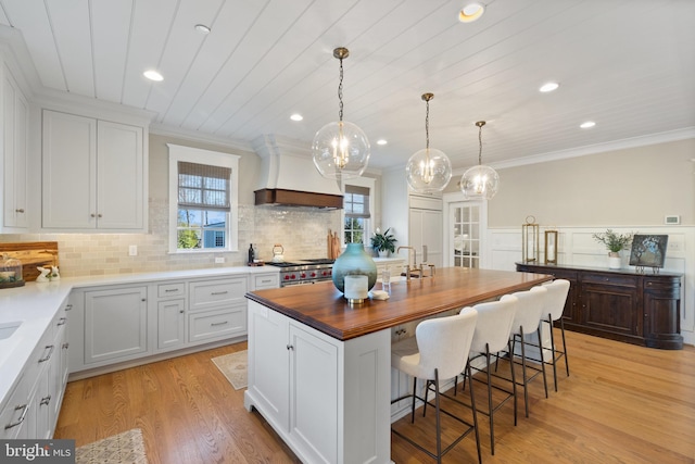 kitchen with premium range hood, a kitchen island, white cabinetry, a kitchen bar, and hanging light fixtures