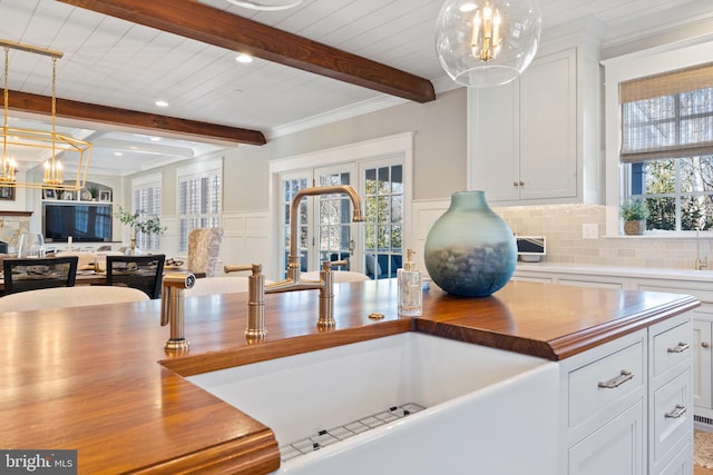 kitchen featuring a healthy amount of sunlight, butcher block counters, sink, and white cabinets