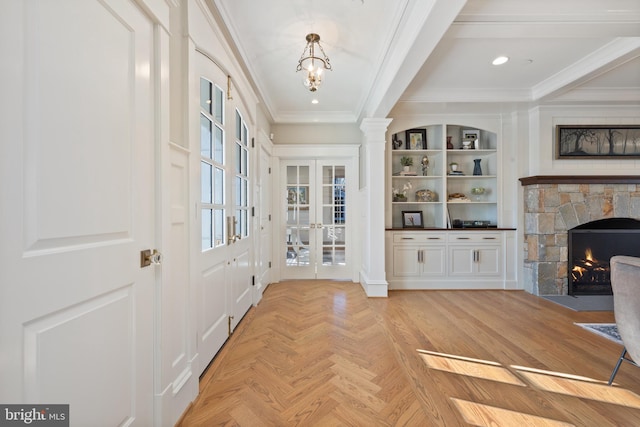 foyer with crown molding, light parquet flooring, a stone fireplace, and french doors