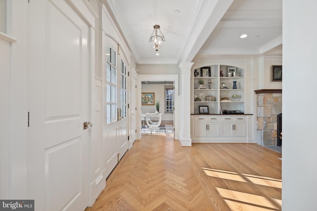 foyer featuring ornate columns, a fireplace, crown molding, a notable chandelier, and light parquet flooring