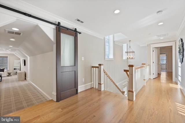 hall featuring a notable chandelier, ornamental molding, a barn door, and light wood-type flooring