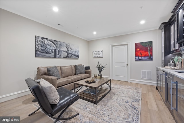 living room featuring crown molding, indoor bar, and light wood-type flooring