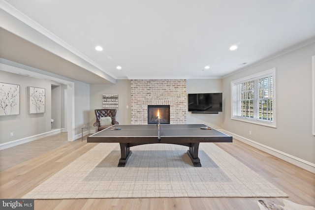 game room featuring a brick fireplace, ornamental molding, and light wood-type flooring