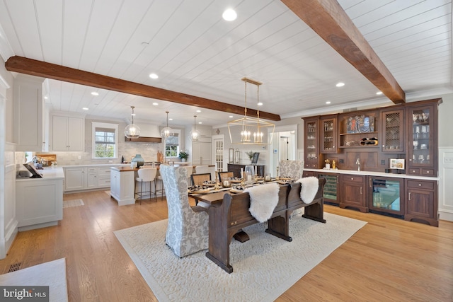 dining area featuring bar area, beverage cooler, beam ceiling, and light hardwood / wood-style floors